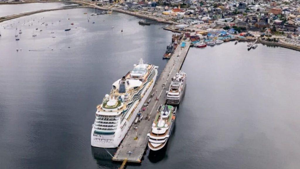 Vista aérea del Puerto de Ushuaia con un crucero y otras embarcaciones amarradas al muelle, junto a la zona urbana de la ciudad