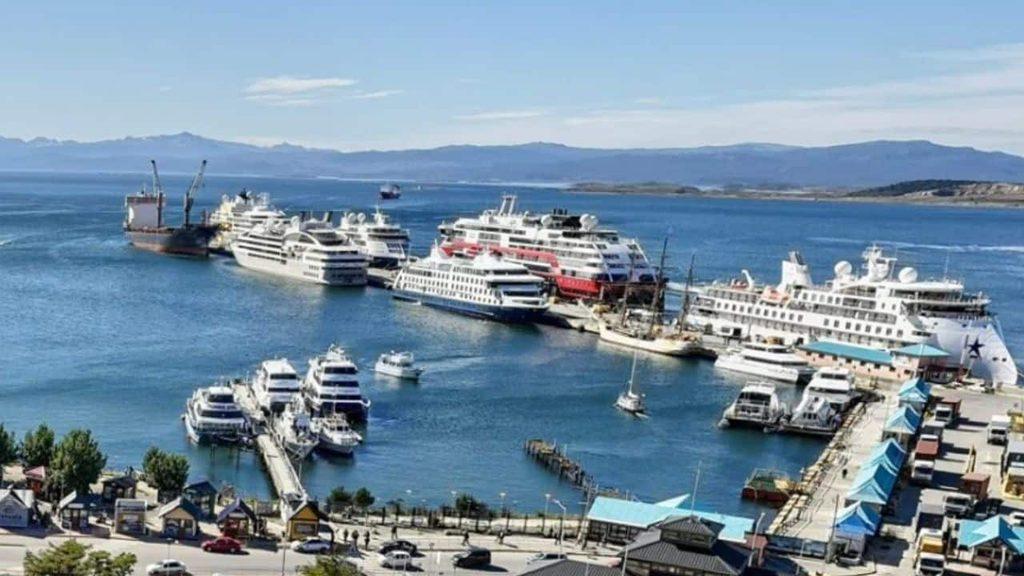 Vista panorámica del Puerto de Ushuaia con cruceros y embarcaciones amarrados en los muelles, rodeados por el canal Beagle y montañas al fondo