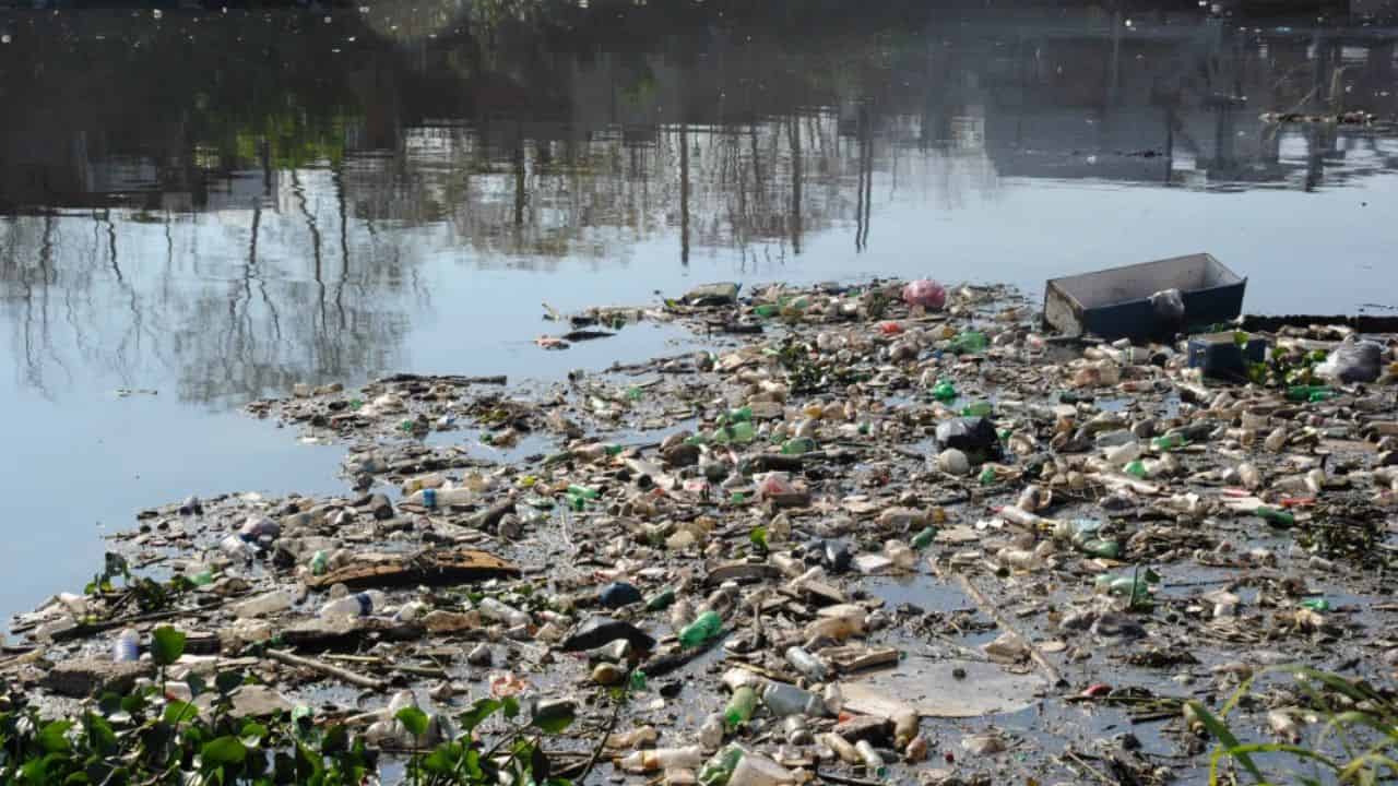 Acumulación de residuos plásticos y basura flotante en la superficie de un curso de agua contaminado
