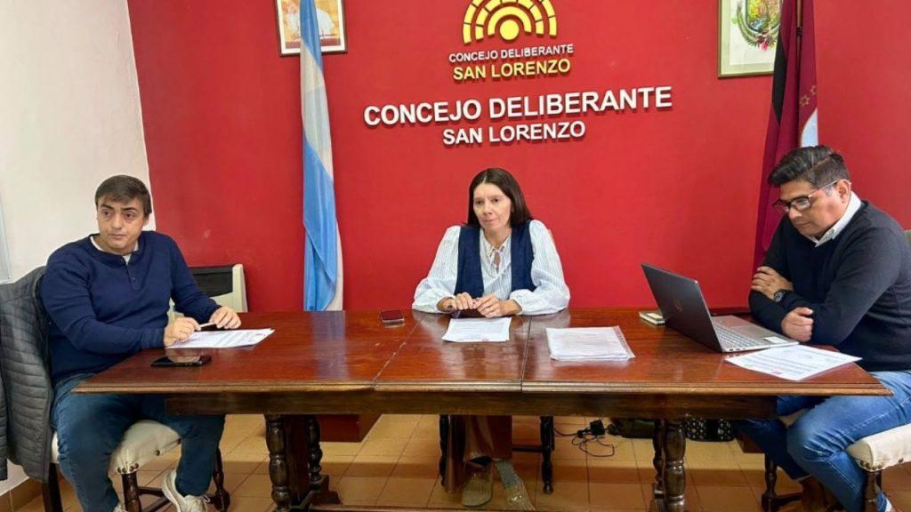 Tres representantes participan de una reunión en el Concejo Deliberante de San Lorenzo, frente al panel institucional del recinto
