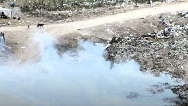 Basural a cielo abierto en San Pedro con acumulación de residuos, humo de una quema y un cuerpo de agua cercano