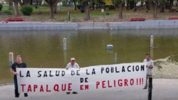 tres personas sostienen una bandera que dice "la salud de la poblacion de tapalque en peligro"